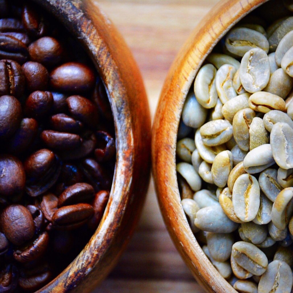 wooden bowls filled with green coffee beans and regular roasted coffee beans 