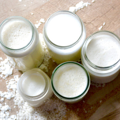 non-dairy milks lined up on a table with coconut shreds, rice grains, and flaxseed