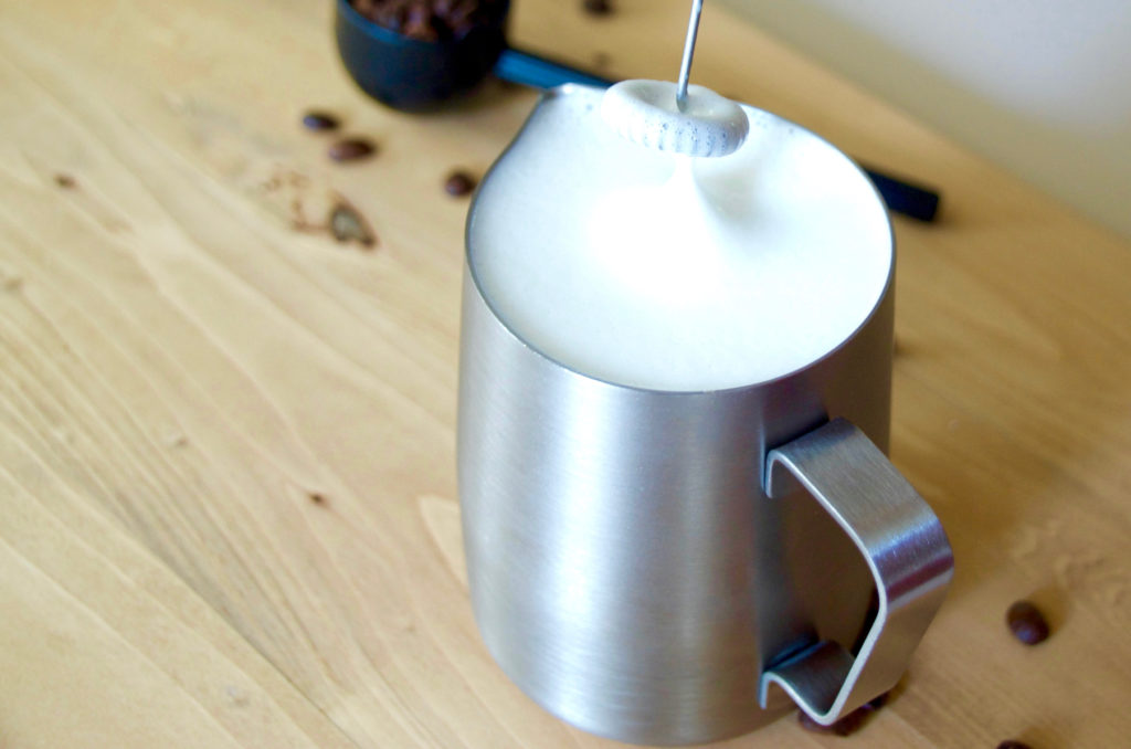 frothing milk in a server with an electric frother on a wooden background