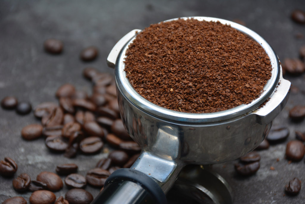 close up of ports filter with coffee grounds on pavement with coffee beans in background