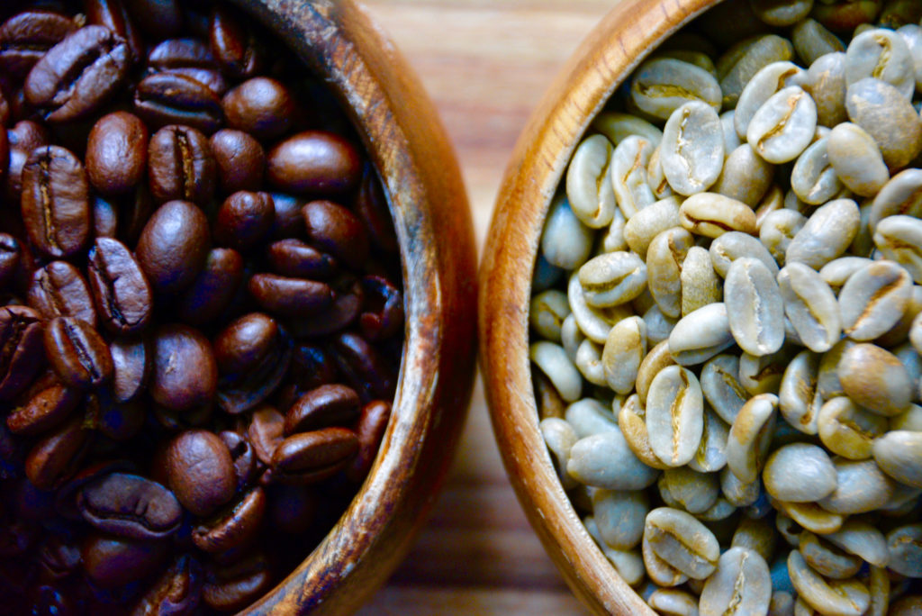 two wooden bowls filled with green beans and roasted coffee beans