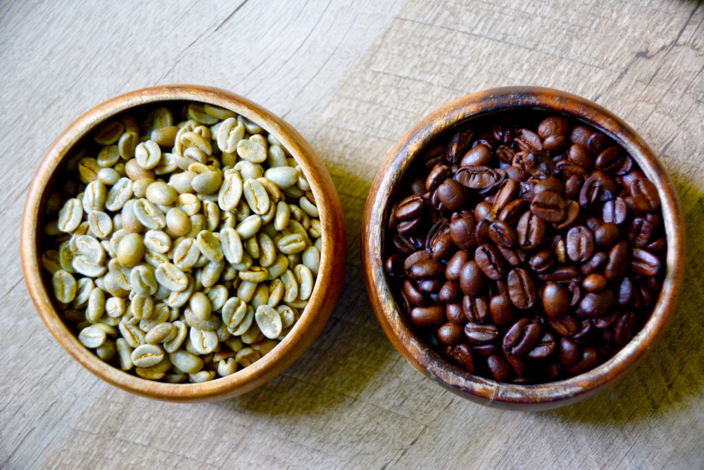 two wooden bowls filled with green beans and roasted coffee beans