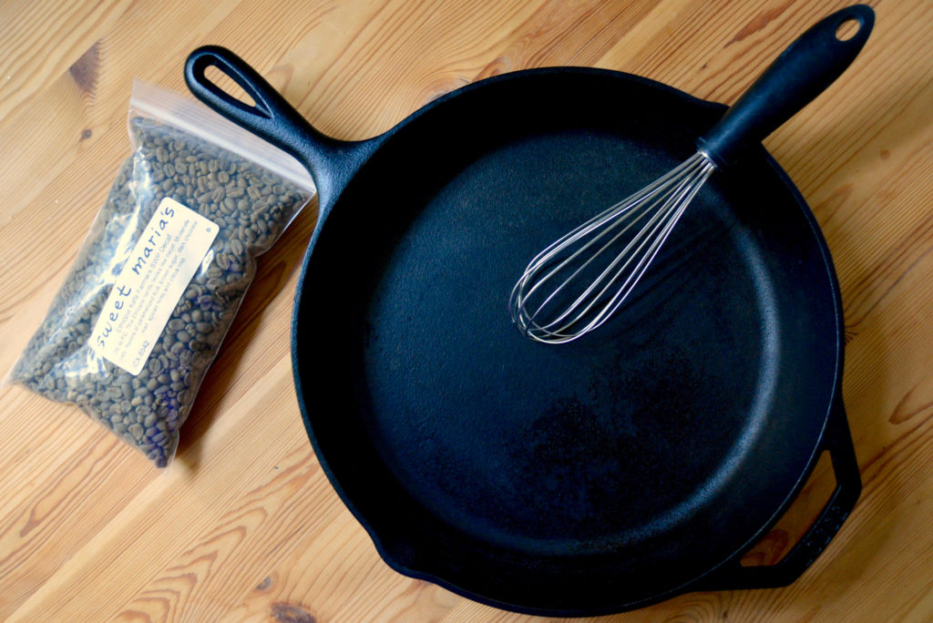 Cast iron pan with metal whisk and green coffee beans on wooden table