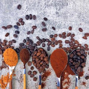 spoons with different coffee beans and roasts on blue background