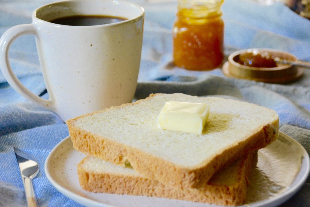 bread with butter and cup of coffee in speckled mug with orange marmalade in background 