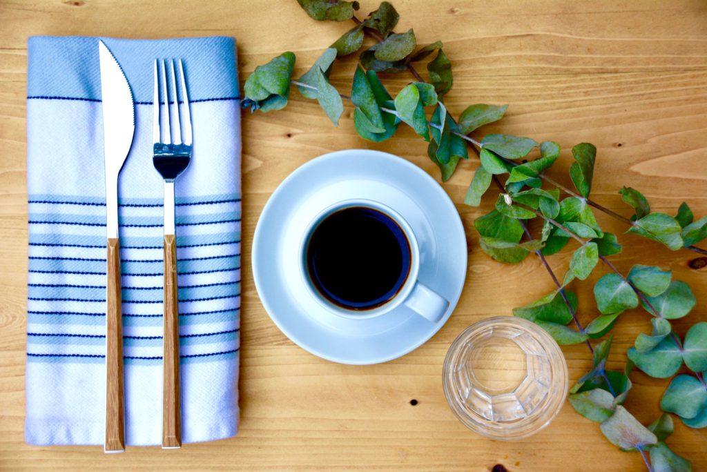 coffee mug on a white saucer on a wood background with eucalyptus 