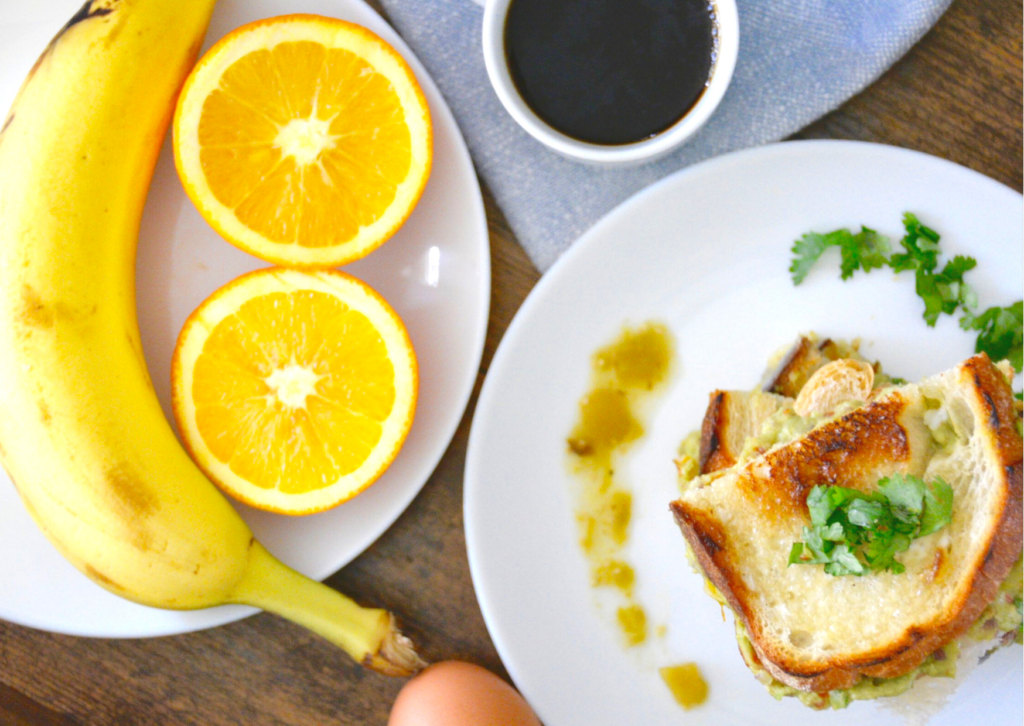 grilled cheese on white plate with coffee and banana and oranges