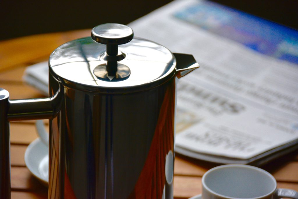 metal French press next to a newspaper on a wooden table