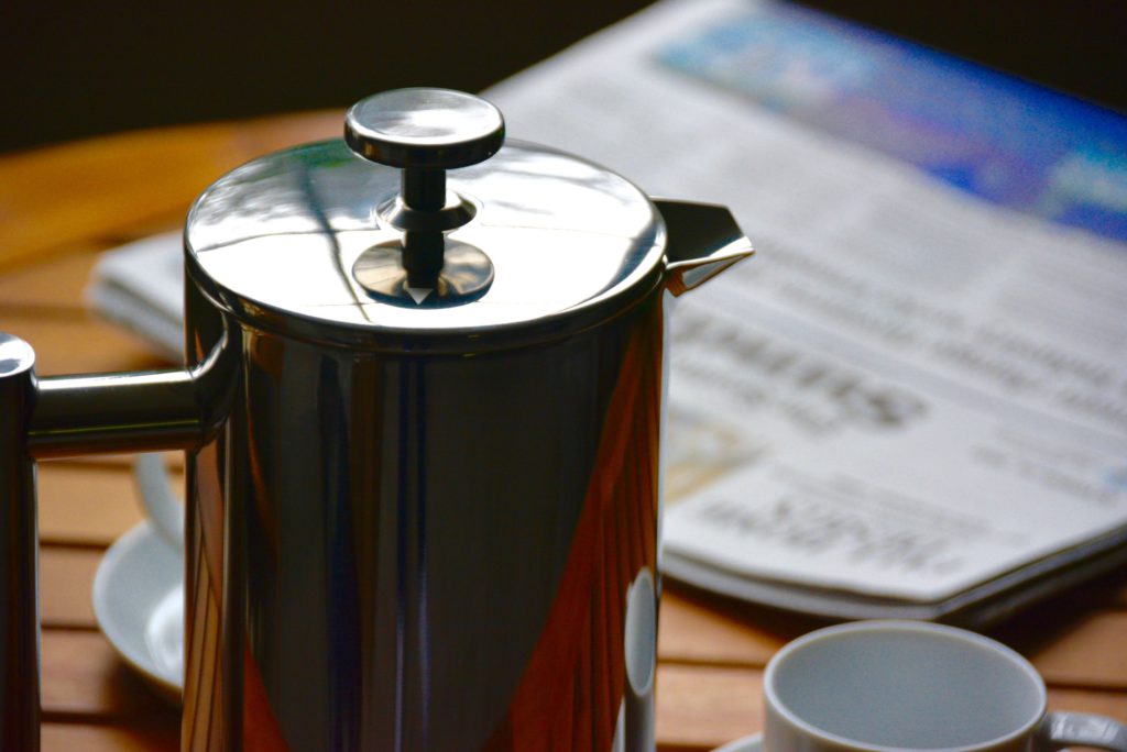 metal French press next to a newspaper on a wooden table 