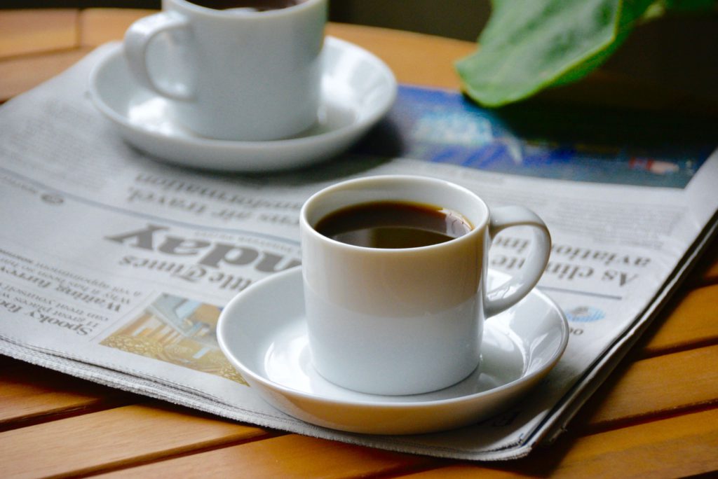 two mini white mugs of coffee on a newspaper