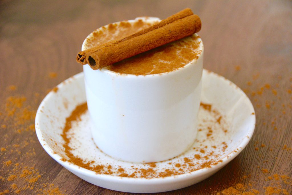chai latte in a white cup with a cinnamon stick