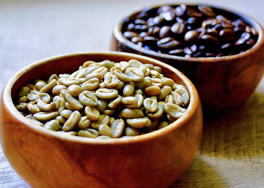 regular coffee beans and green coffee beans in wooden bowls