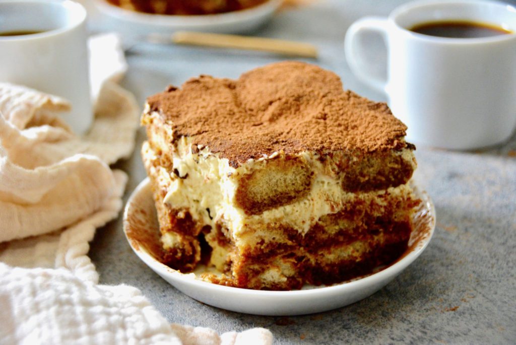 tiramisu close up next to a white mug of coffee